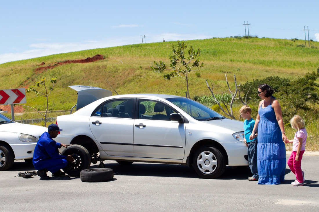 Technician changing car tires while woman and two children watch