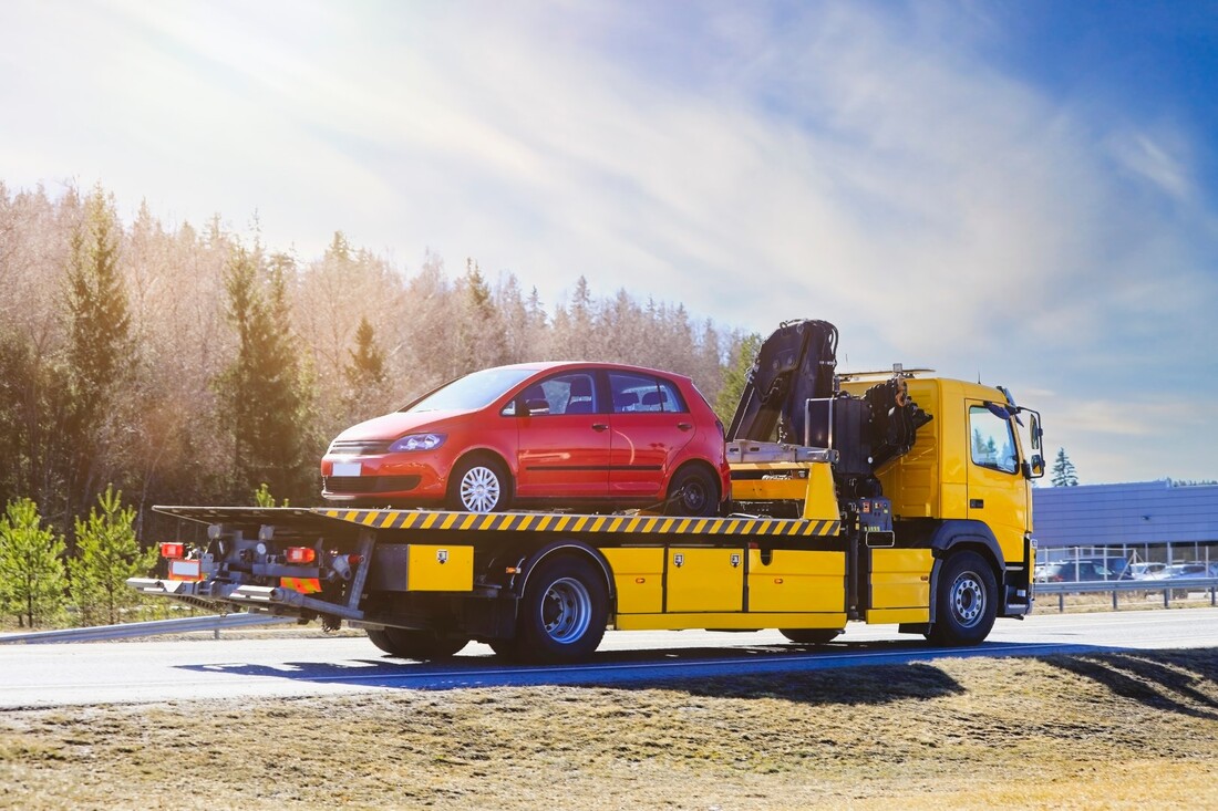Red hatchback being towed by yellow tow truck