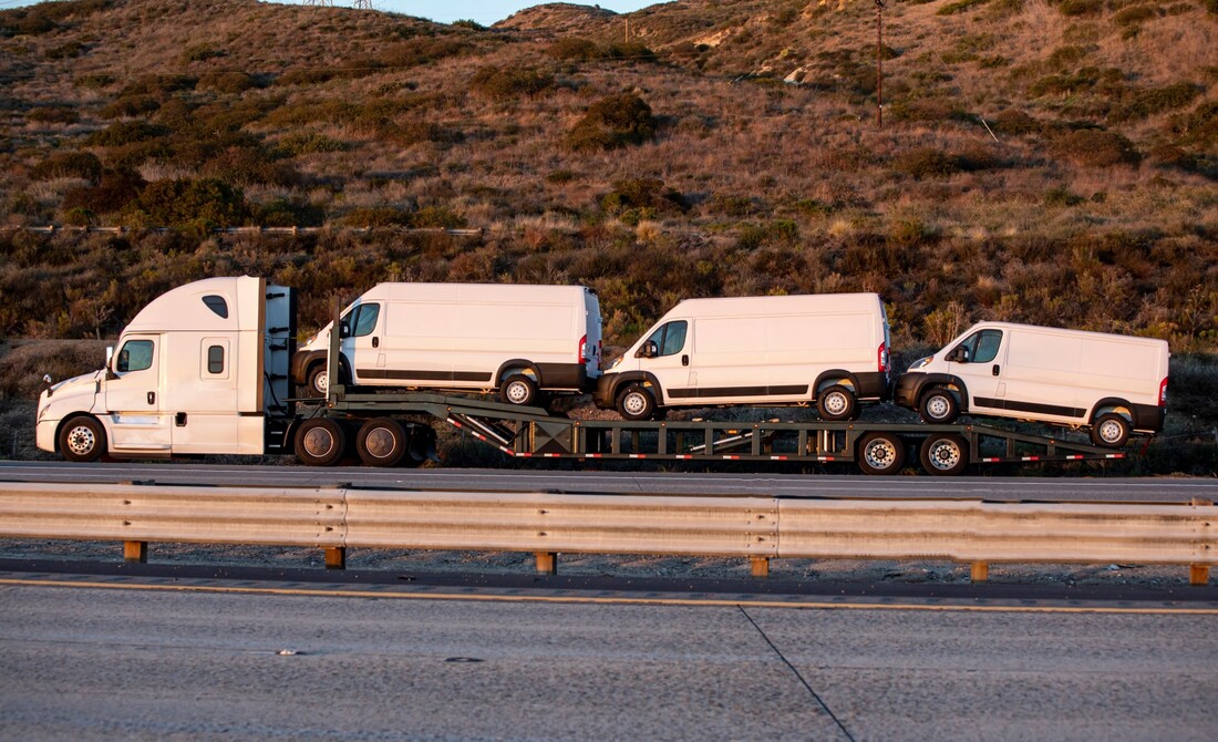 Large flatbed truck towing three white vans